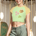 Woman wearing a colorful crop top with a bee design and green pants, standing in front of a decorative background.