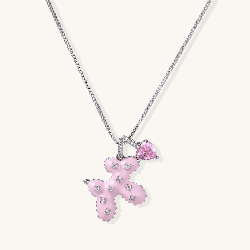 Pink enamel cross pendant with zirconia crystals and teardrop charm on 18K gold-plated chain against white background