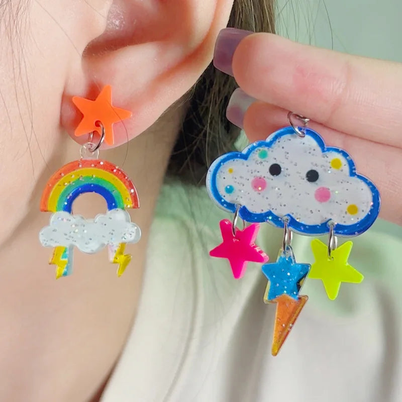 Colorful earrings with rainbows, stars, and clouds worn by a person.