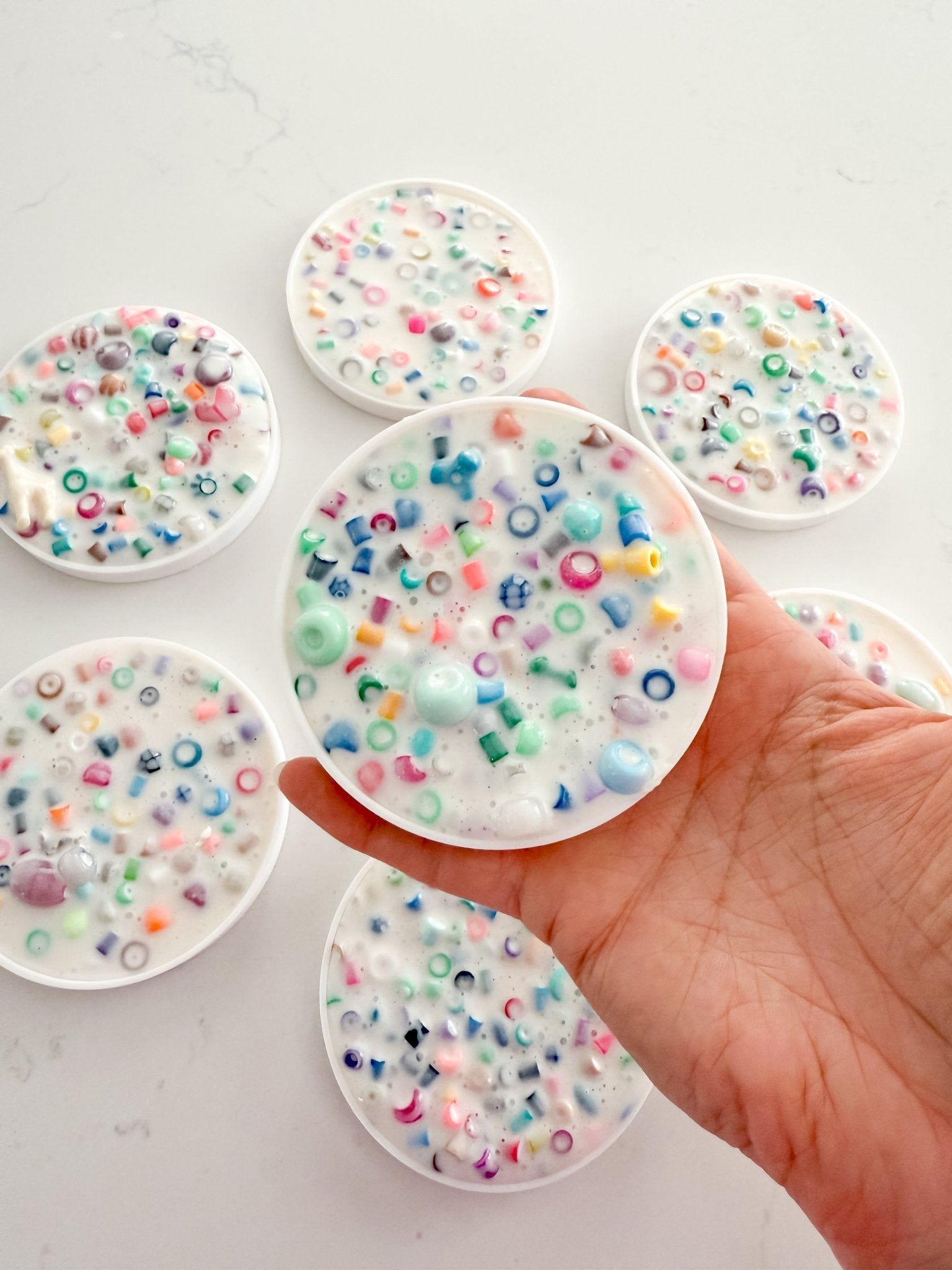 Hand holding a round, white object with colorful beads on a light gray background